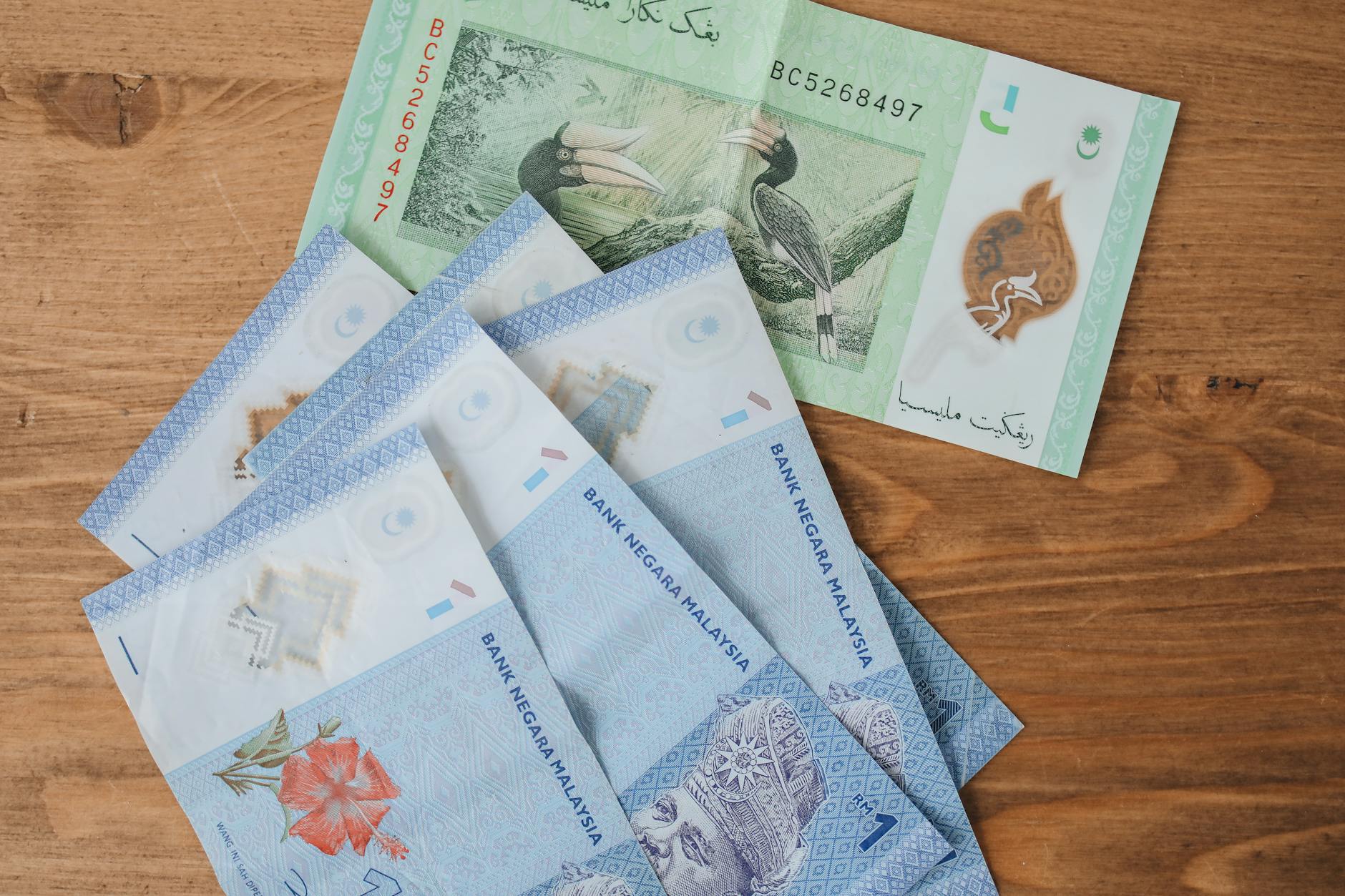 Collection of Malaysian Ringgit banknotes in various denominations displayed on a wooden background.
